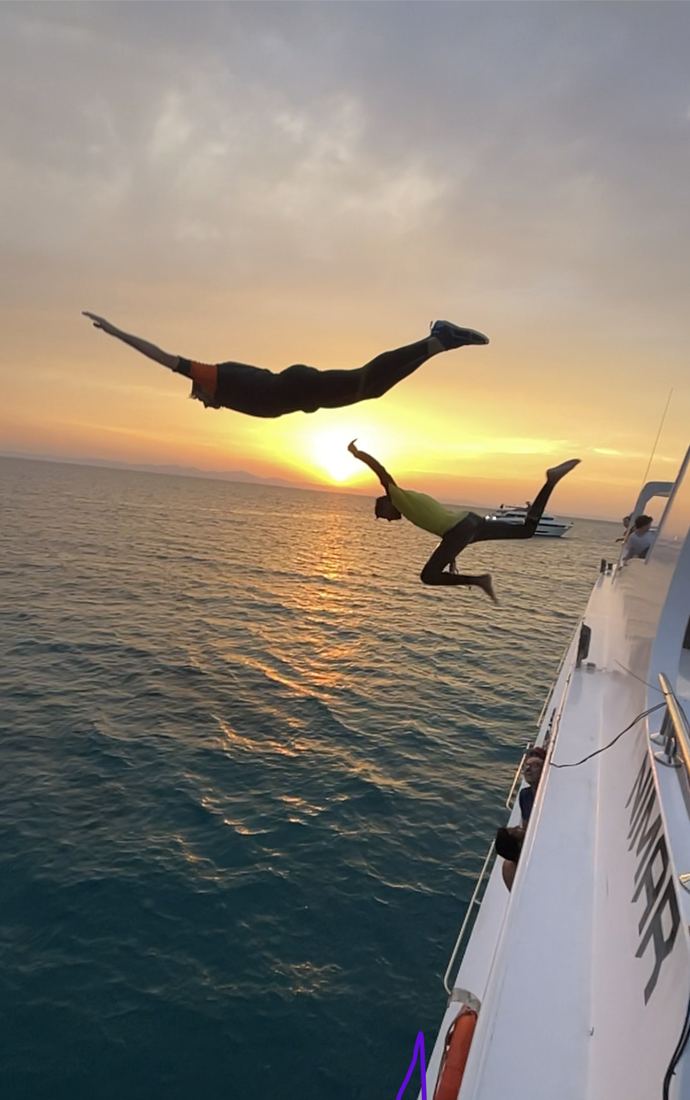 Zwei Personen springen bei Sonnenuntergang vom Boot ins Rote Meer