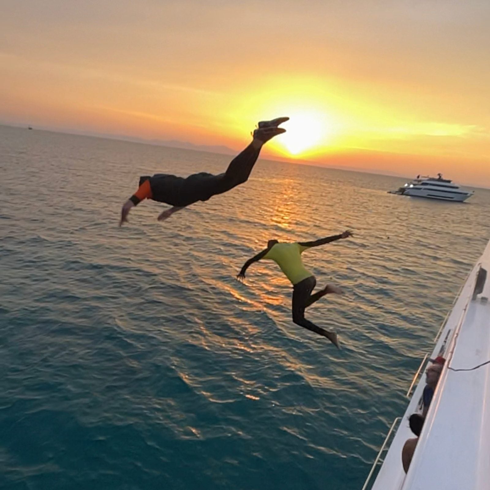 Zwei Personen springen bei Sonnenuntergang vom Boot ins Wasser